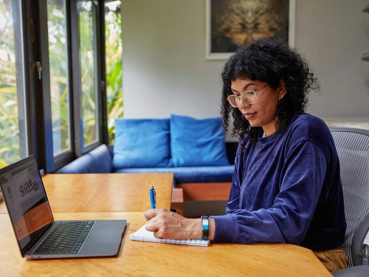 A woman working at a laptop at her dining table by a window