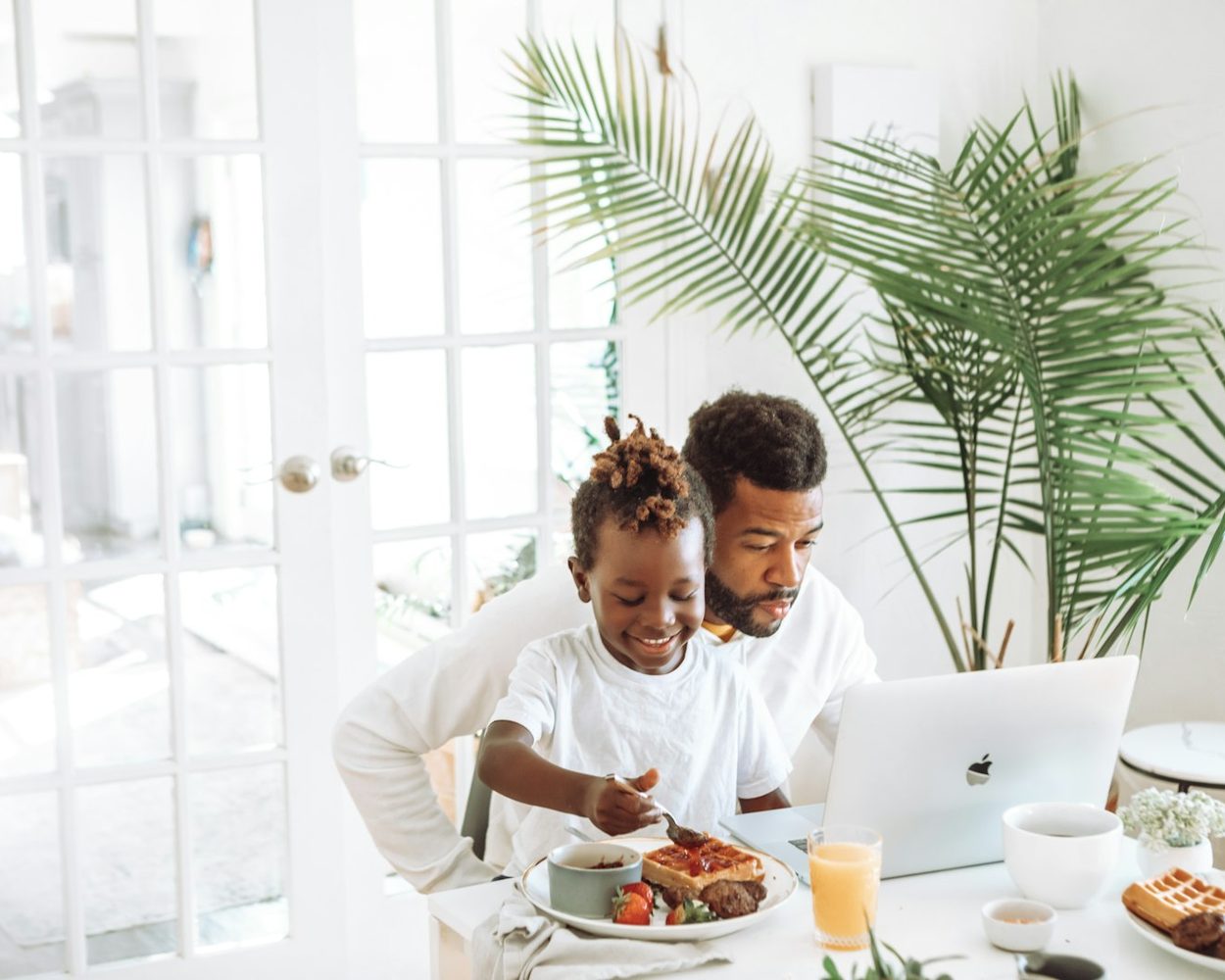 A father and his young son having breakfast beside an open laptop